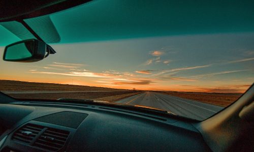 Car driving on open highway at sunset, view from dashboard, clear sky, scenic horizon.