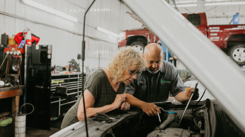 Mechanic showing woman car engine details in auto repair shop.