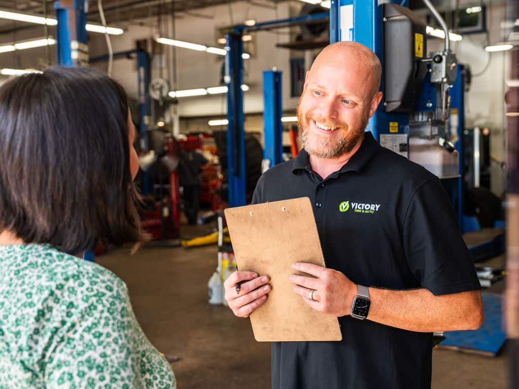 Friendly mechanic talking to a customer in an auto repair shop, holding a clipboard.