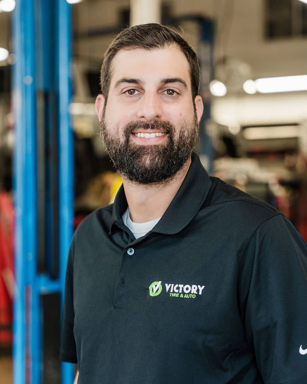 Smiling man in Victory Tire & Auto polo shirt standing in an auto shop.