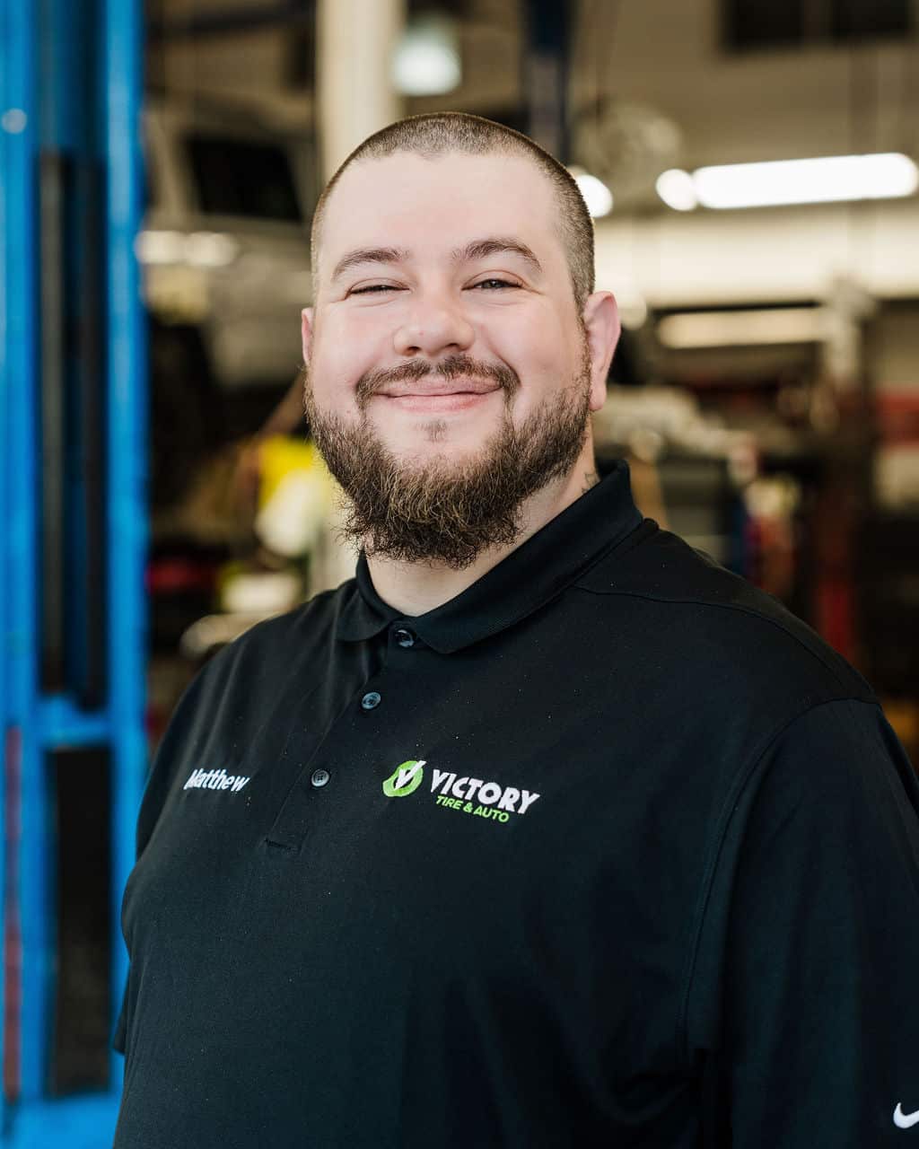 Smiling mechanic in Victory Tire & Auto uniform standing in an automotive workshop.