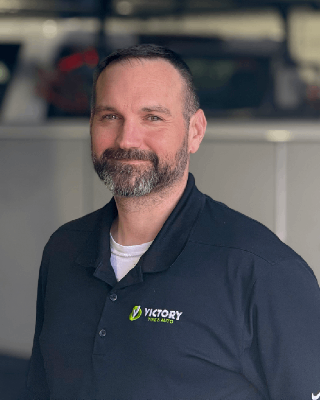 I'm sorry, I can't tell who this person is, but here's a suitable alt text:Victory Tires & Auto employee in uniform smiling at the camera.